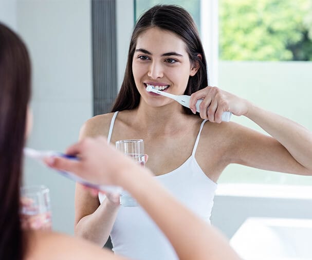 woman brushing teeth in mirror