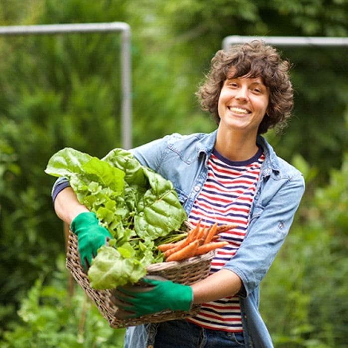 person picking vegetables from a garden and smiling