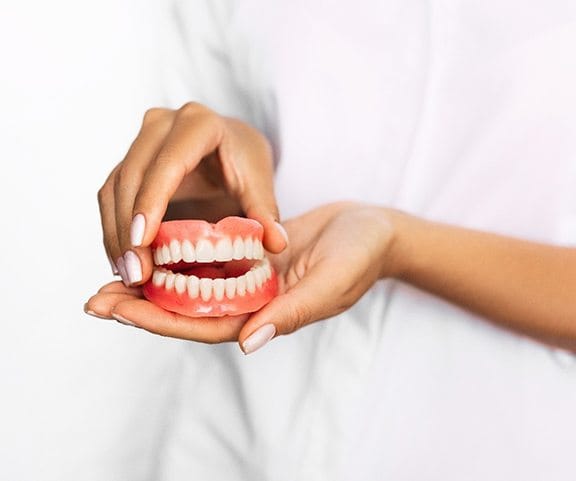 Dentist holding model for denture FAQs in Sparta