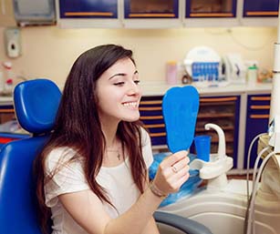 Woman using mirror at emergency dental office in Sparta