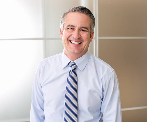 older man in blue shirt and tie smiling