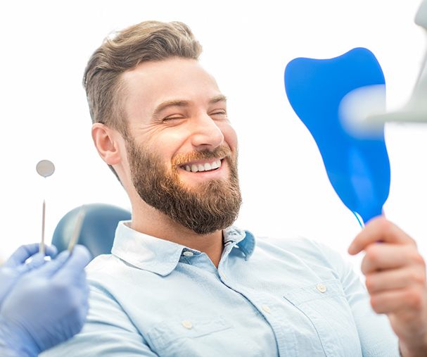 man smiling while looking in dental mirror