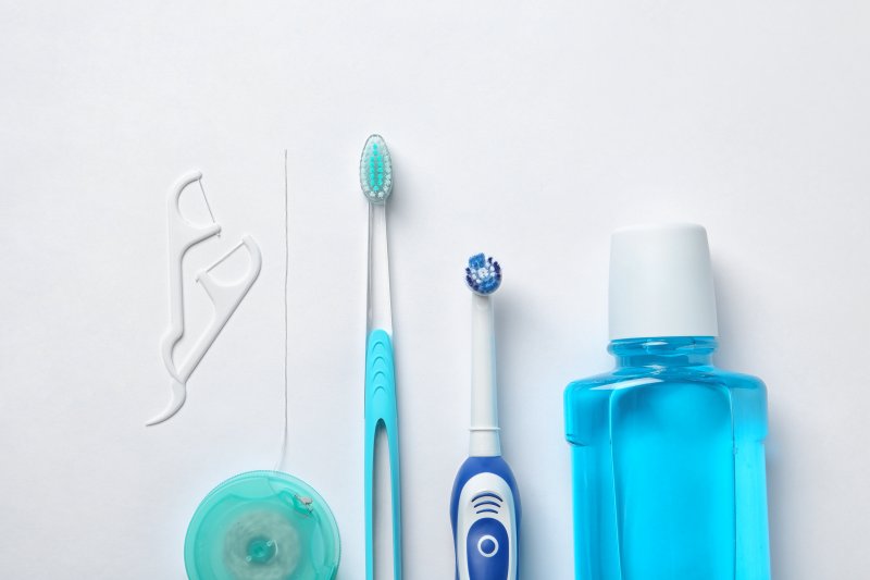 an image of dental floss, two types of toothbrushes, and mouthwash 