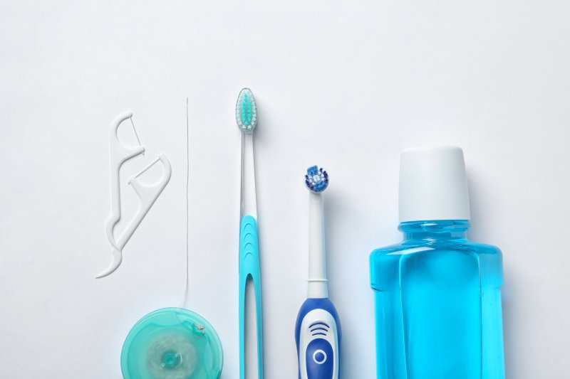 an image of dental floss, two types of toothbrushes, and mouthwash