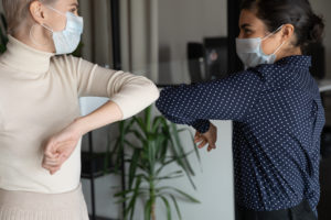 Two women wearing face masks and bumping elbows