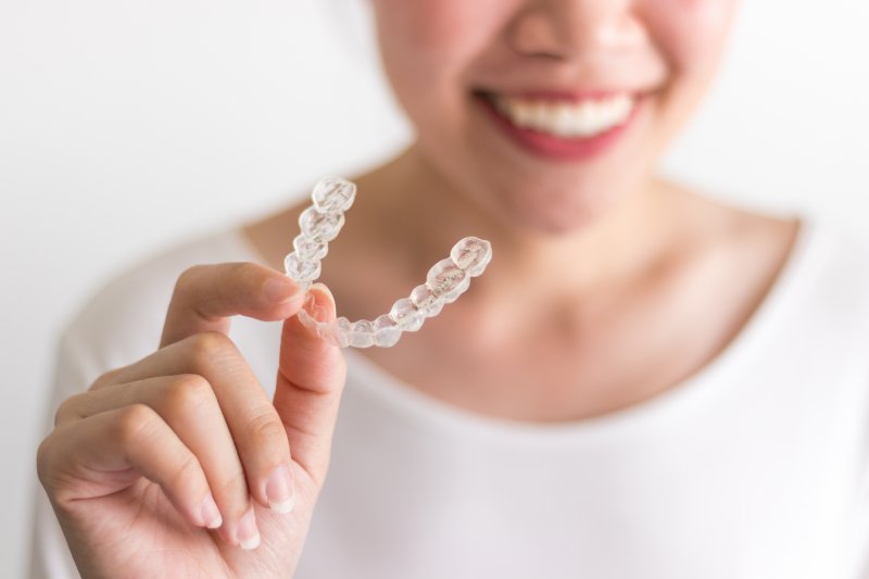 person smiling and holding Invisalign aligner