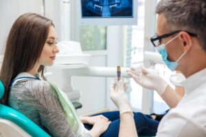 Dentist explaining dental implant model to young woman patient.