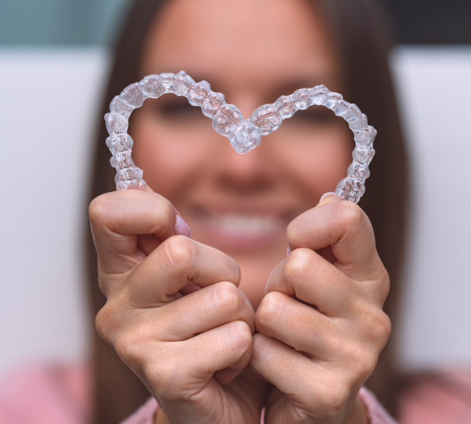 Woman holding clear aligners in heart shape
